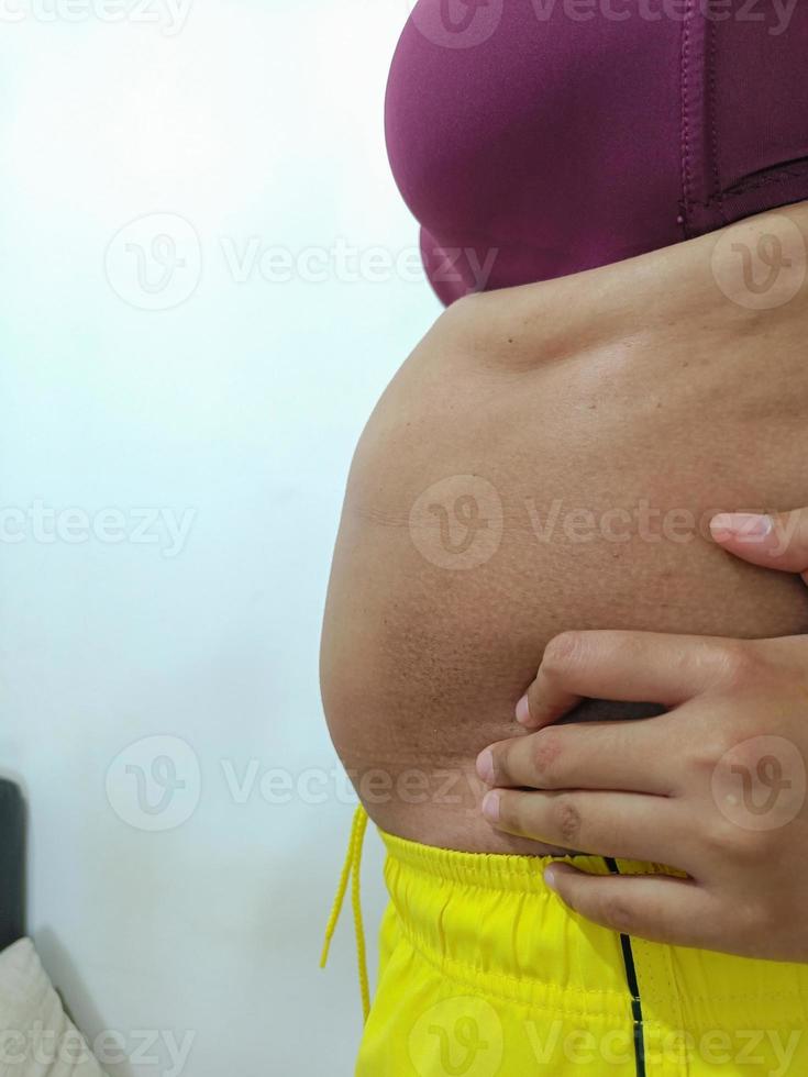 vista lateral. mulher asiática gorda em pé mostrando sua barriga foto