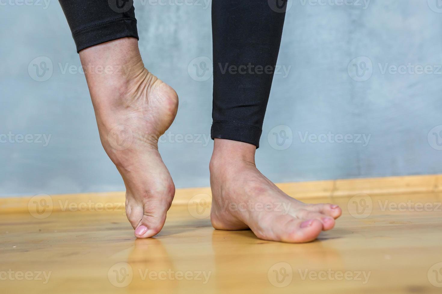 pés femininos descalços em leggings pretas em um piso de madeira foto