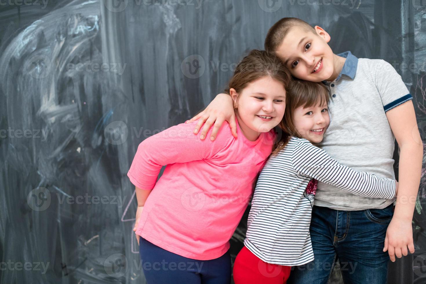 grupo de crianças abraçando na frente do quadro-negro foto