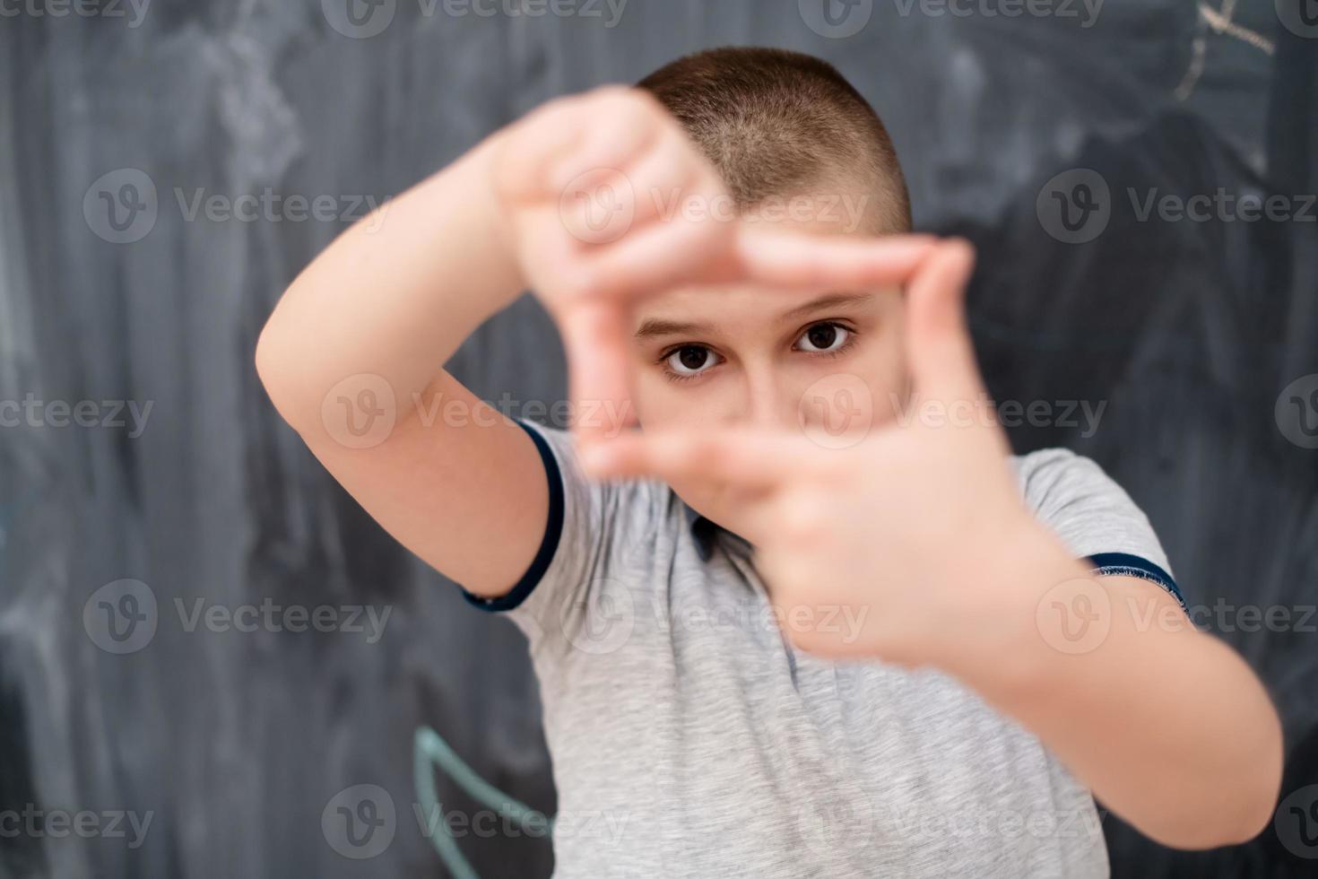 menino feliz fazendo gesto de moldura de mão na frente do quadro-negro foto