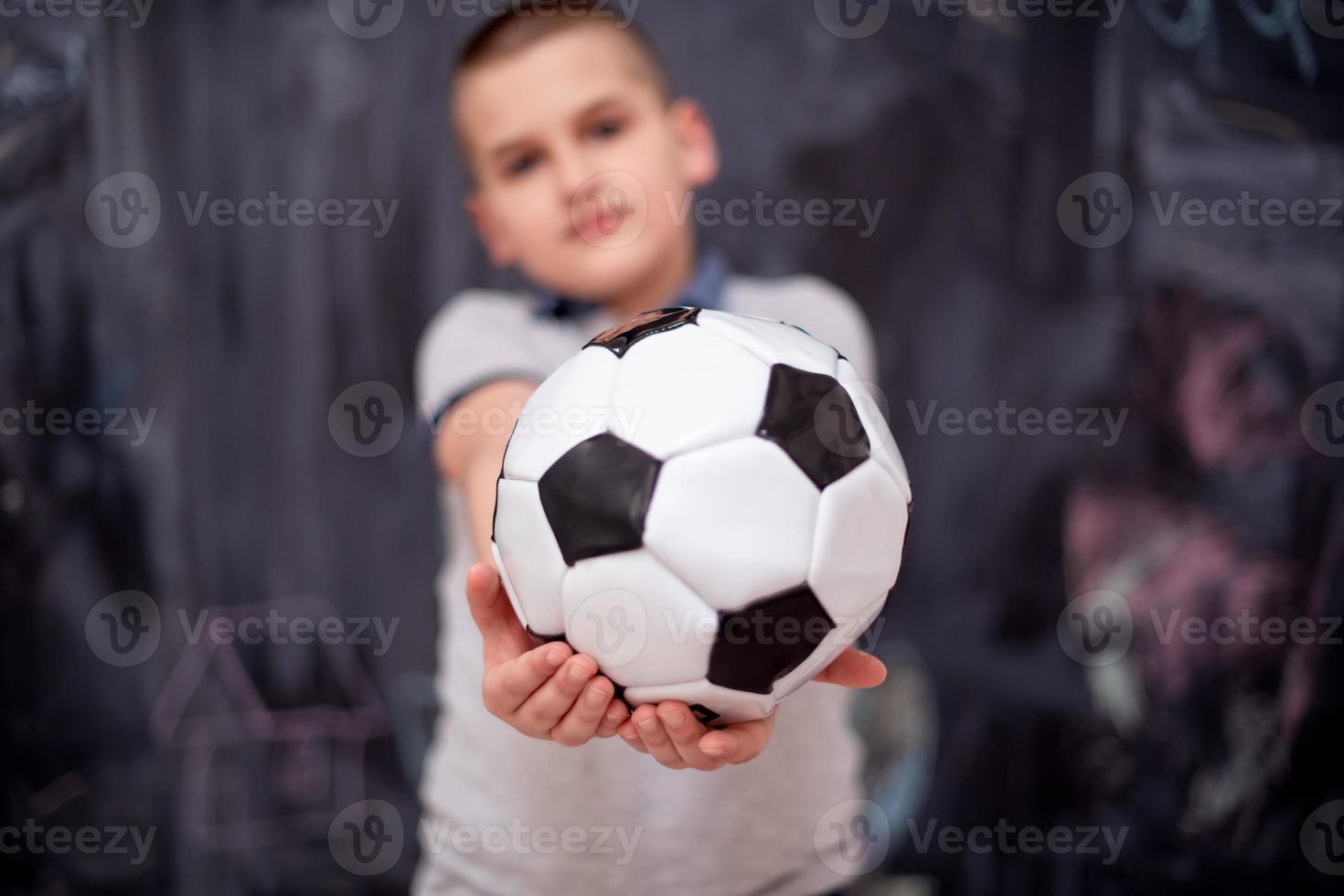 menino feliz segurando uma bola de futebol na frente do quadro-negro foto