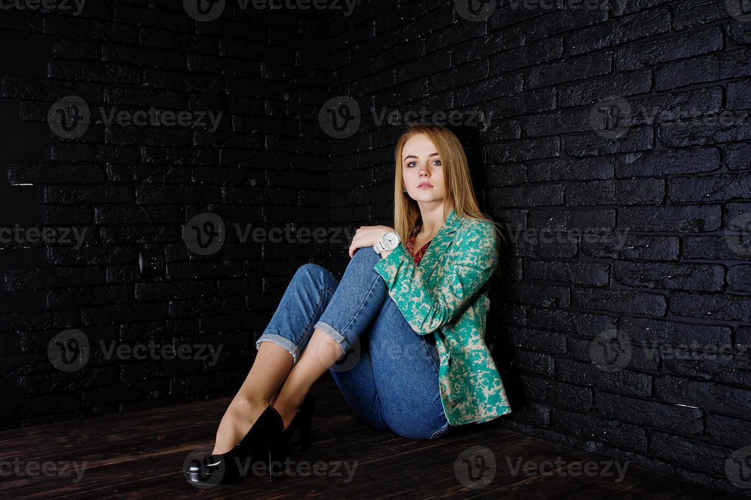 menina loira elegante jaqueta e jeans contra a parede de tijolo preto no estúdio. foto