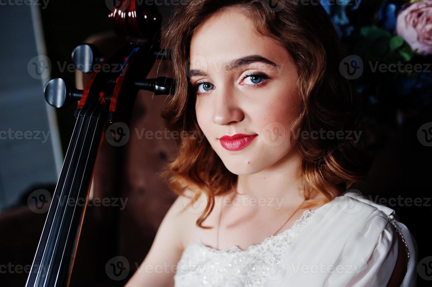 músico muito jovem gilrl vestido branco com contrabaixo sentado no sofá vintage marrom. foto