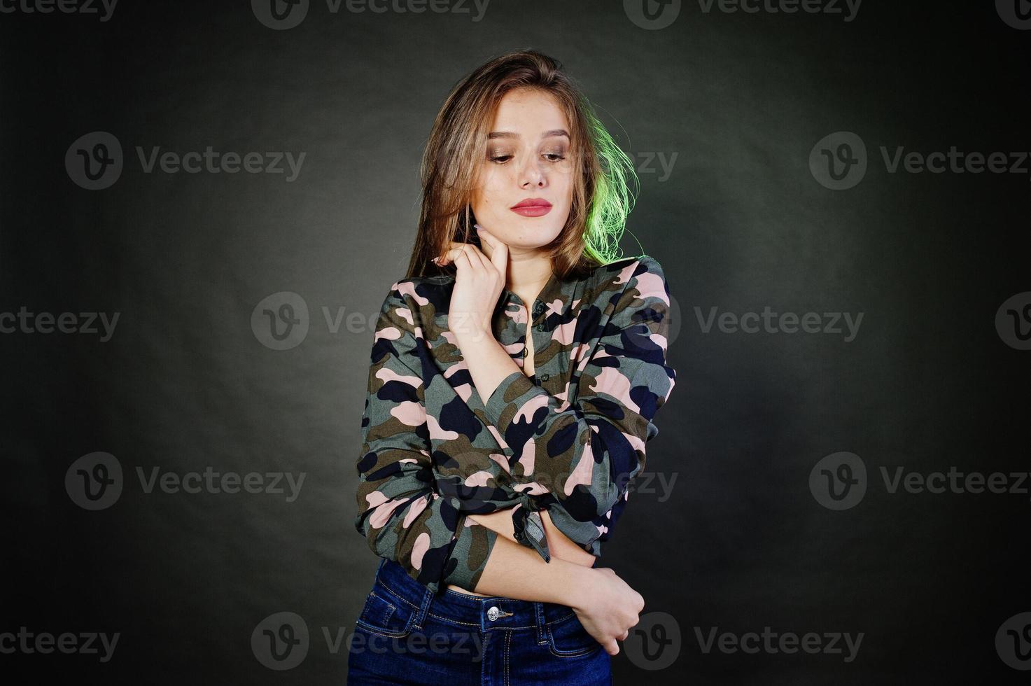 menina morena bonita usa calça jeans e camisa militar, posando no estúdio contra um fundo cinza. retrato de modelo de estúdio. foto