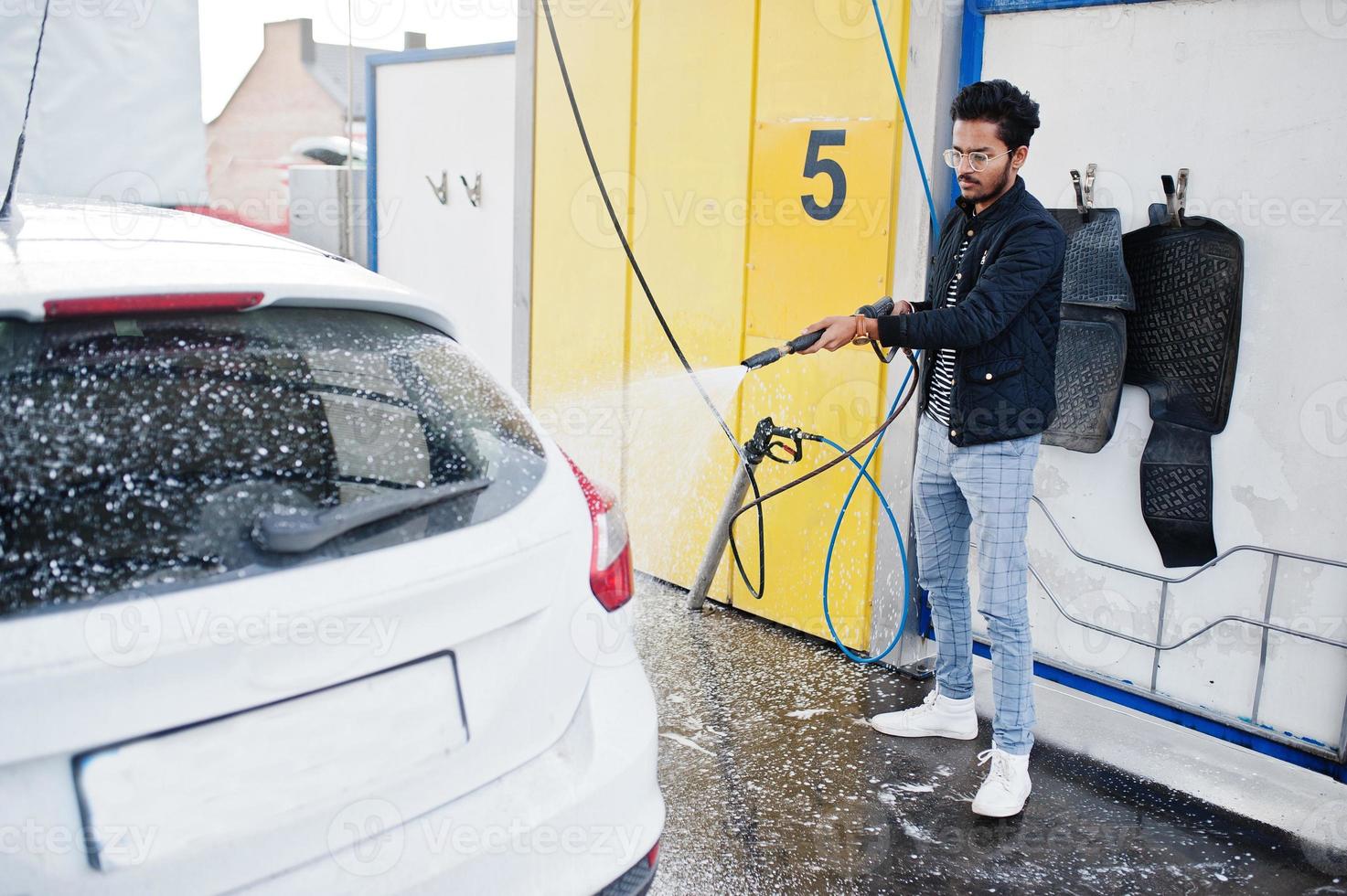 homem do sul da Ásia ou homem indiano lavando seu transporte branco na lavagem de carros. foto