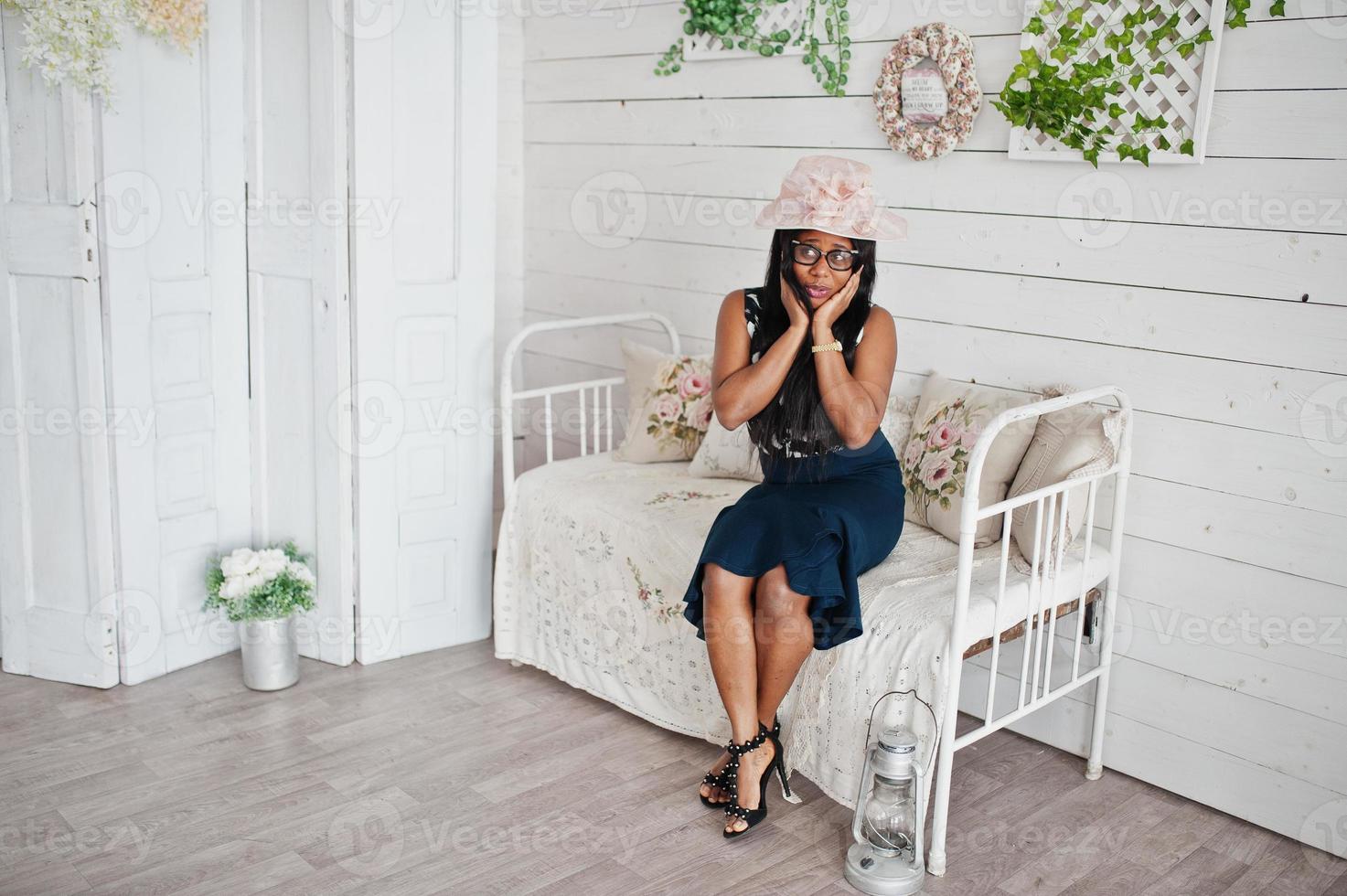 linda mulher afro-americana de óculos e chapéu posou no quarto sentado no sofá vintage. foto