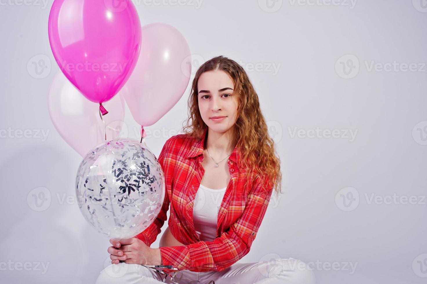 jovem de camisa vermelha e calça branca com balões contra fundo branco no estúdio. foto