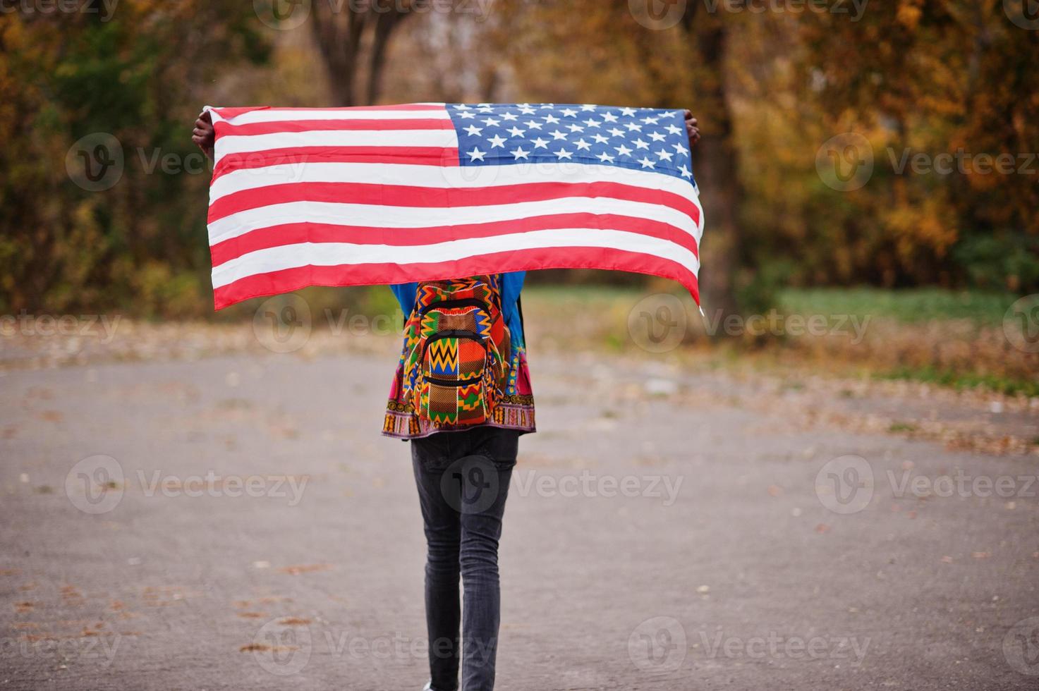 homem africano na camisa tradicional da África no parque outono com bandeira dos eua. foto