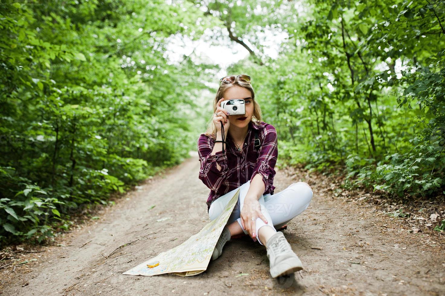 retrato de uma loira atraente com um mapa sentado na floresta e tirando fotos. foto