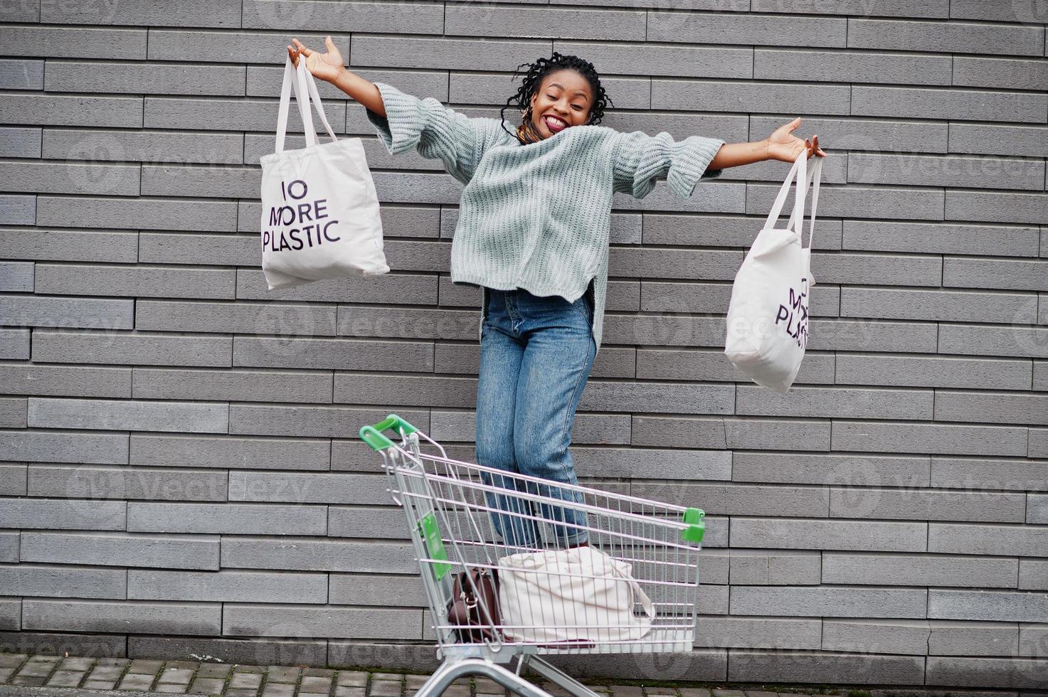 não mais plástico. mulher africana com carrinho de compras e sacolas ecológicas saltam no mercado ao ar livre. foto