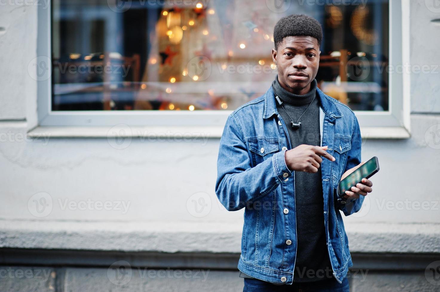 homem africano usar jaqueta jeans posou ao ar livre com o celular na mão. foto