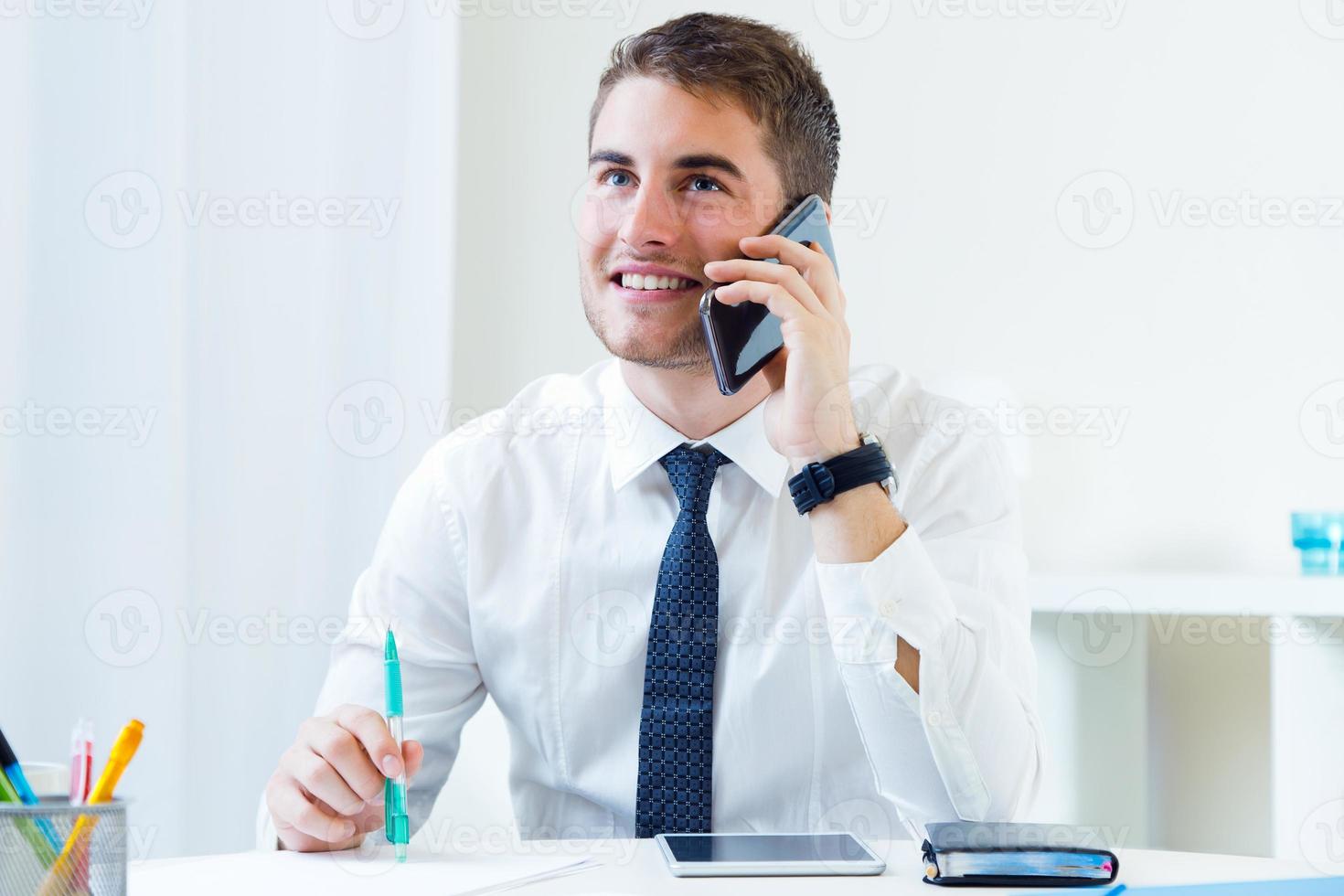 jovem bonito, trabalhando em seu escritório com telefone móvel. foto