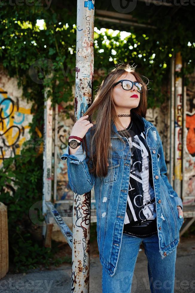 garota elegante hipster casual em jeans e óculos contra a grande parede de graffiti. foto