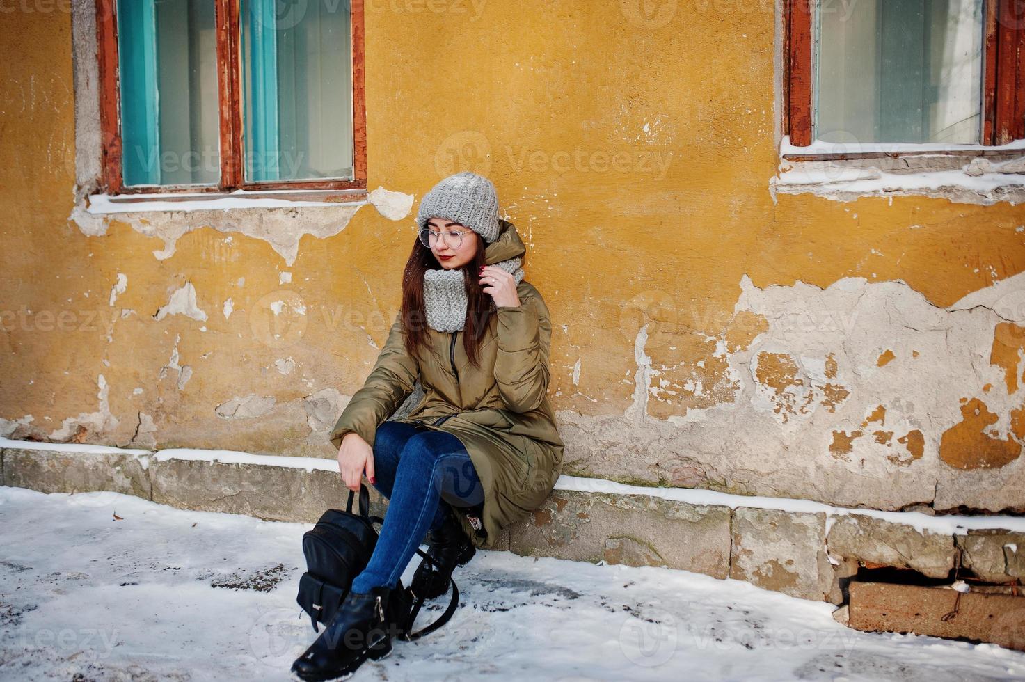 retrato de menina morena de cachecol cinza e chapéu, óculos no tempo frio contra a parede laranja da casa velha. foto