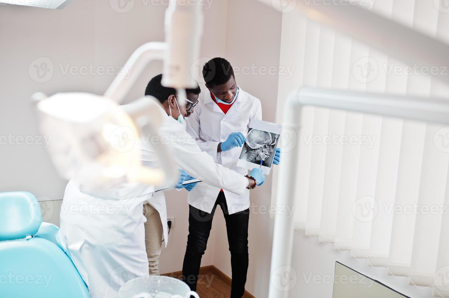 três médicos afro-americanos trabalhando, discutindo com colegas na clínica e apontam no crânio de raio-x. foto