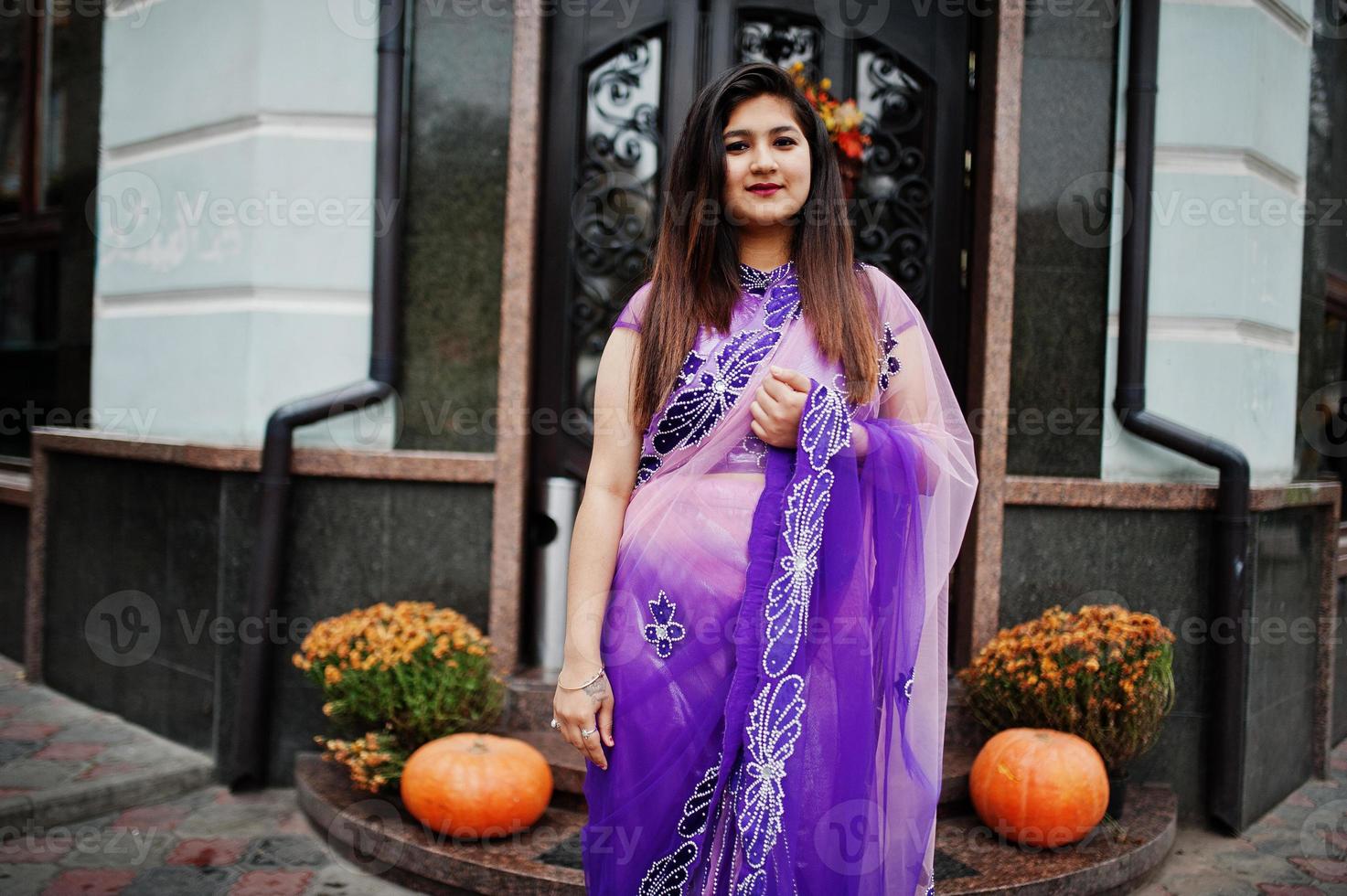 garota hindu indiana no tradicional saree violeta posou na rua contra a porta do restaurante com clima de outono e abóboras. foto