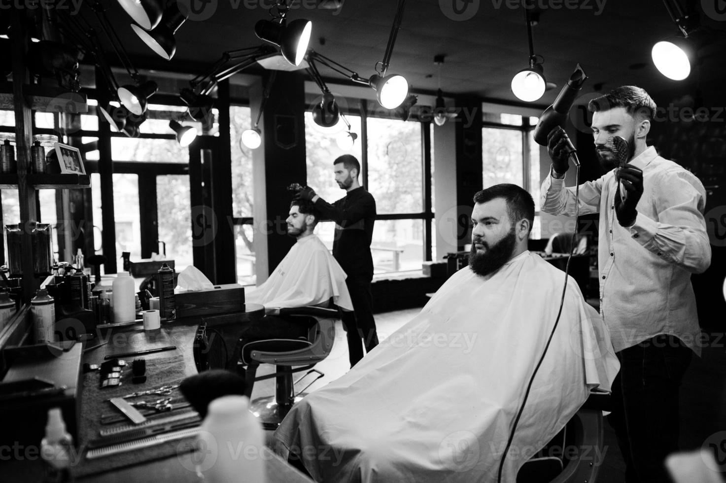 homem barbudo bonito na barbearia, barbeiro no trabalho, usando secador de cabelo. foto