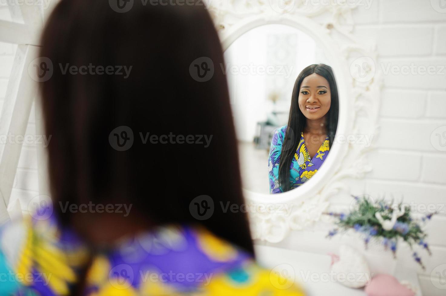 elegância modelo de mulher afro-americana usar roupas coloridas. mulheres afro chiques no quarto olhando no espelho. foto