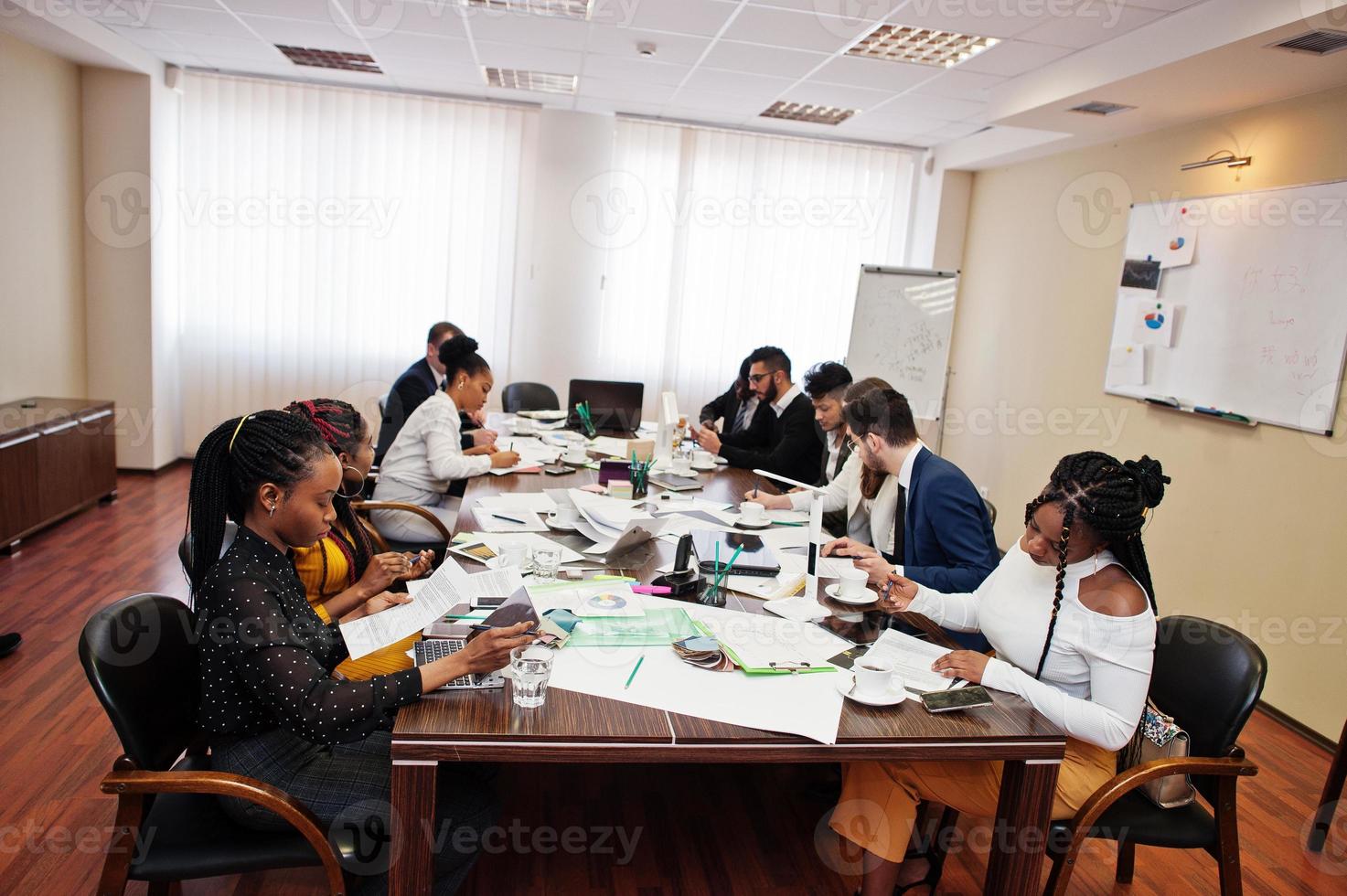 equipe de negócios multirracial abordando a reunião em torno da mesa da diretoria, trabalhando juntos e escrevendo algo em papéis. foto