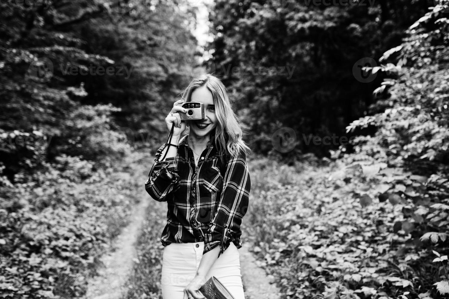 retrato de uma linda jovem na camisa tartan tirando fotos com a câmera na floresta.