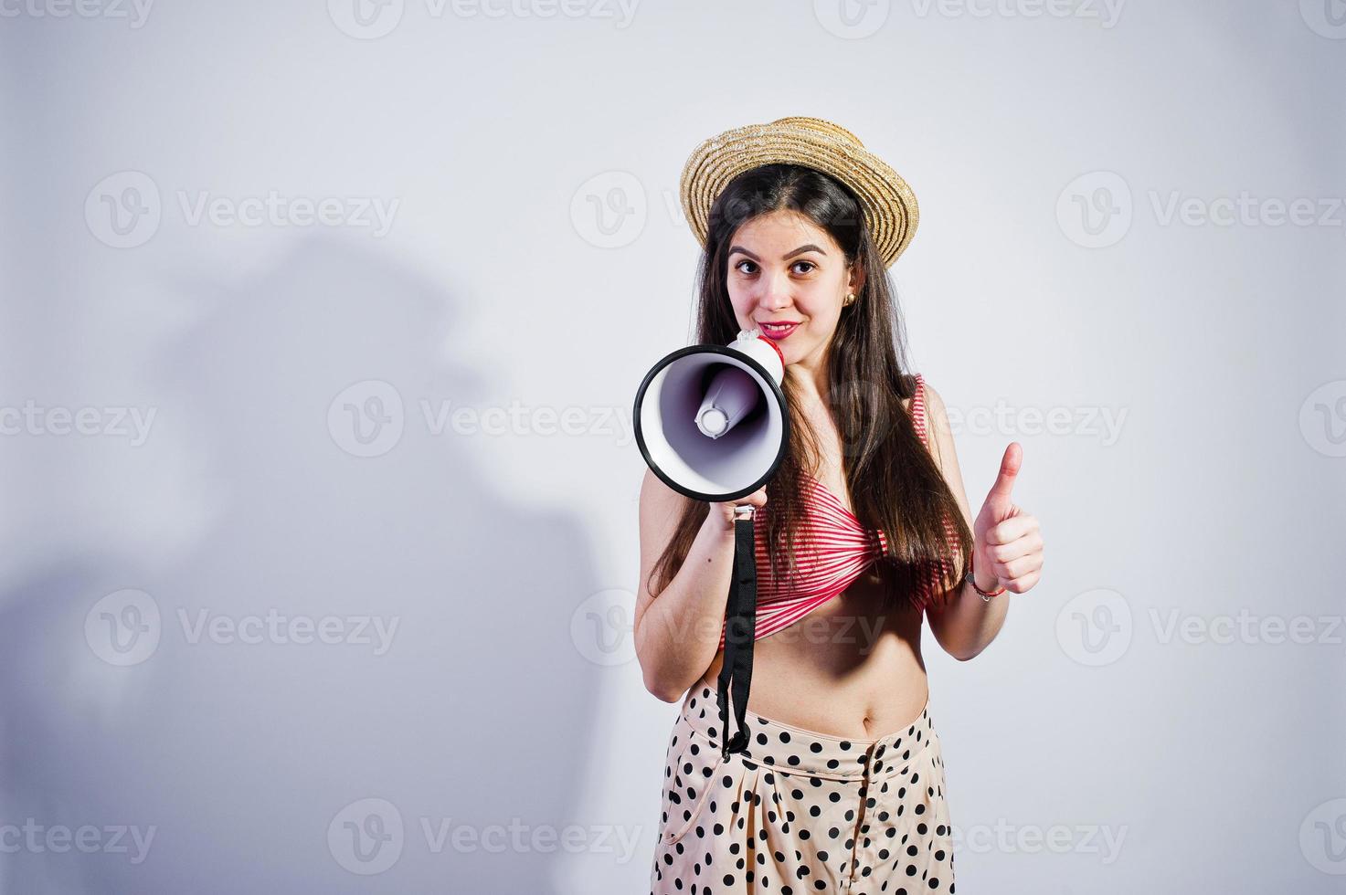 retrato de uma linda jovem em traje de banho e chapéu fala em megafone no estúdio. foto