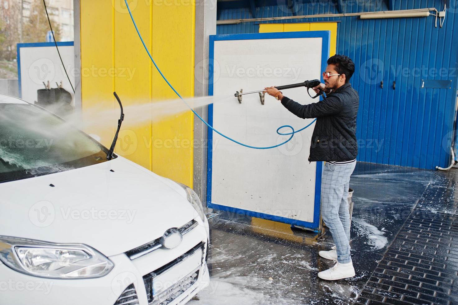 homem do sul da Ásia ou homem indiano lavando seu transporte branco na lavagem de carros. foto