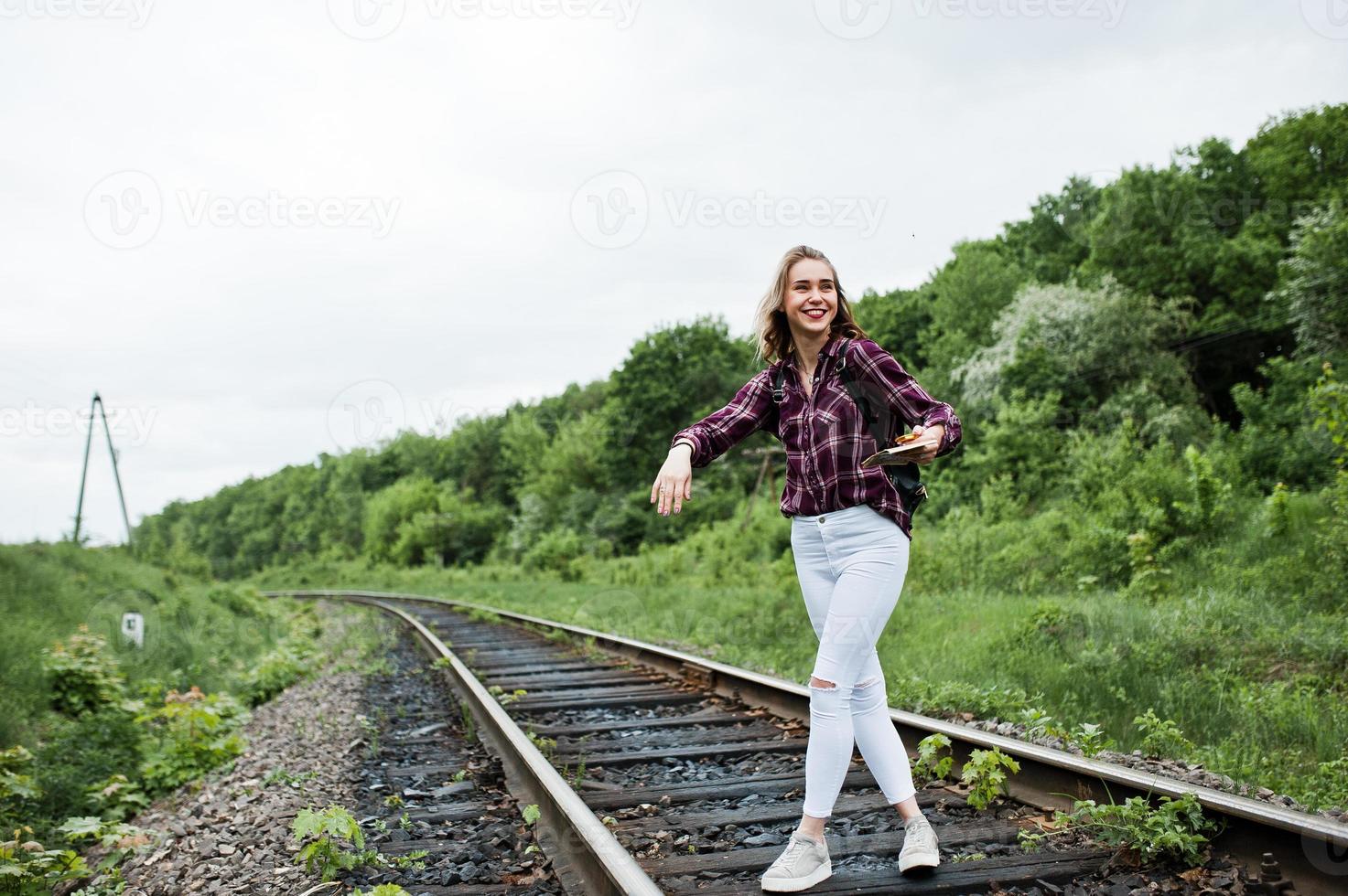 retrato de uma menina bonita loira na camisa tartan andando na ferrovia com mapa nas mãos dela. foto