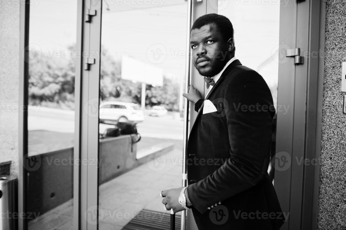 homem afro-americano elegante bonito com roupa formal e gravata borboleta com bengala. foto