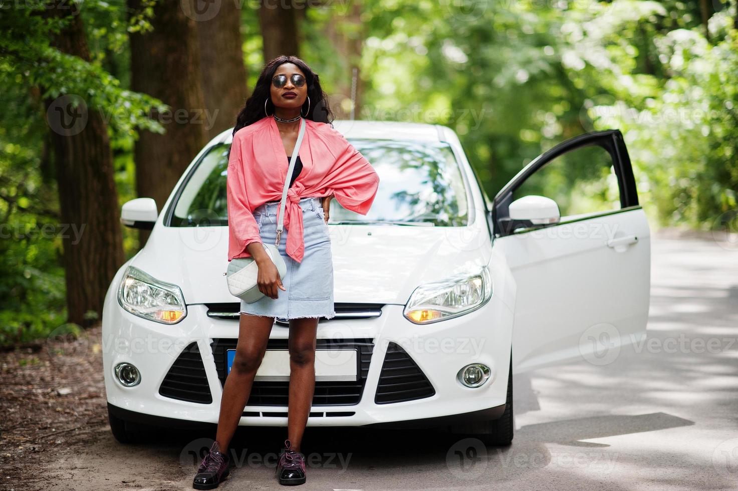 mulher afro-americana posou contra carro branco na estrada florestal. foto