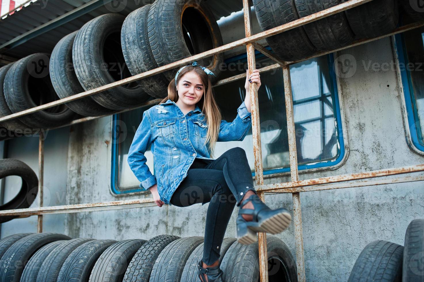 garota jovem hippie na jaqueta jeans e lenço na cabeça na zona de montagem do pneu. foto