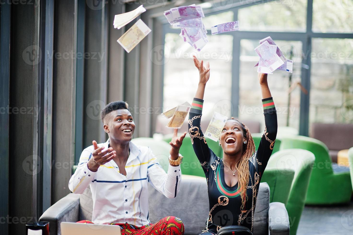 bonito elegante casal americano africano sentado no escritório junto com o laptop e dinheiro. dinheiro no ar. foto