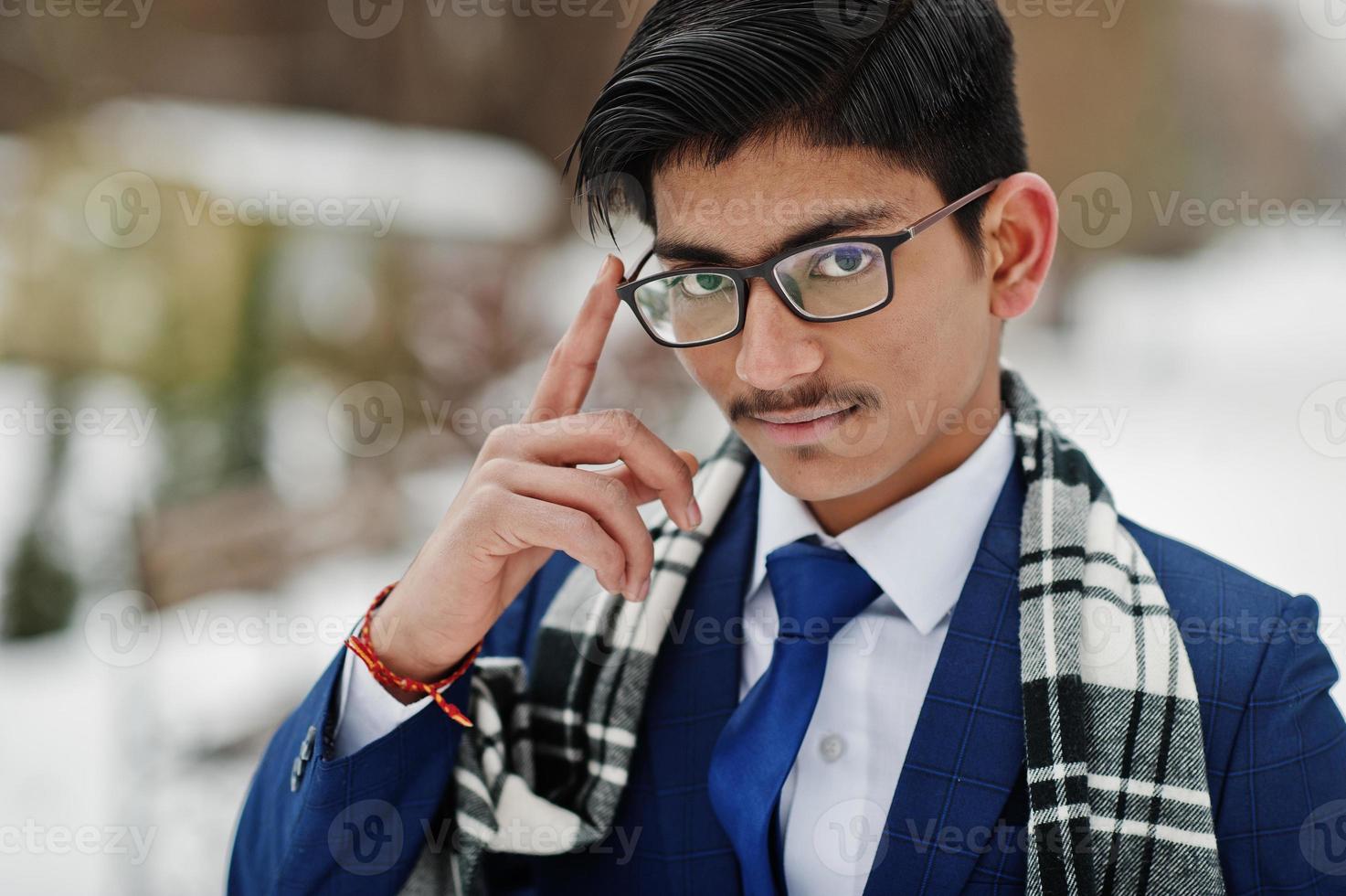 Feche o retrato do homem elegante estudante indiano de terno, óculos e cachecol posou no dia de inverno ao ar livre. foto