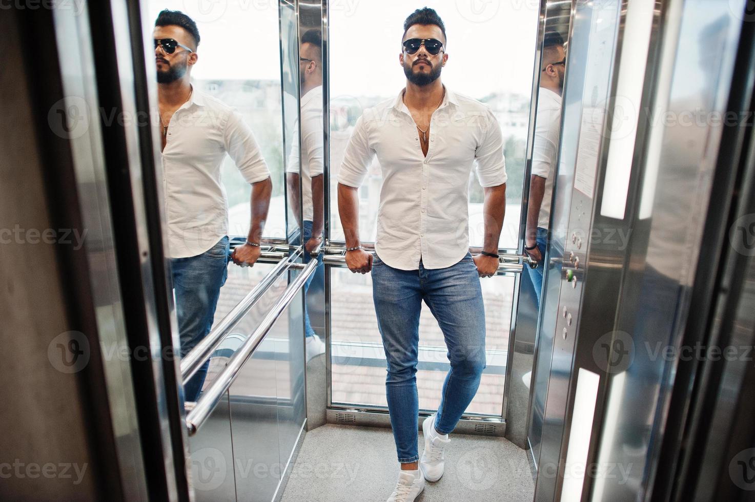 elegante modelo de homem árabe alto na camisa branca, jeans e óculos de sol posou no elevador dentro. foto