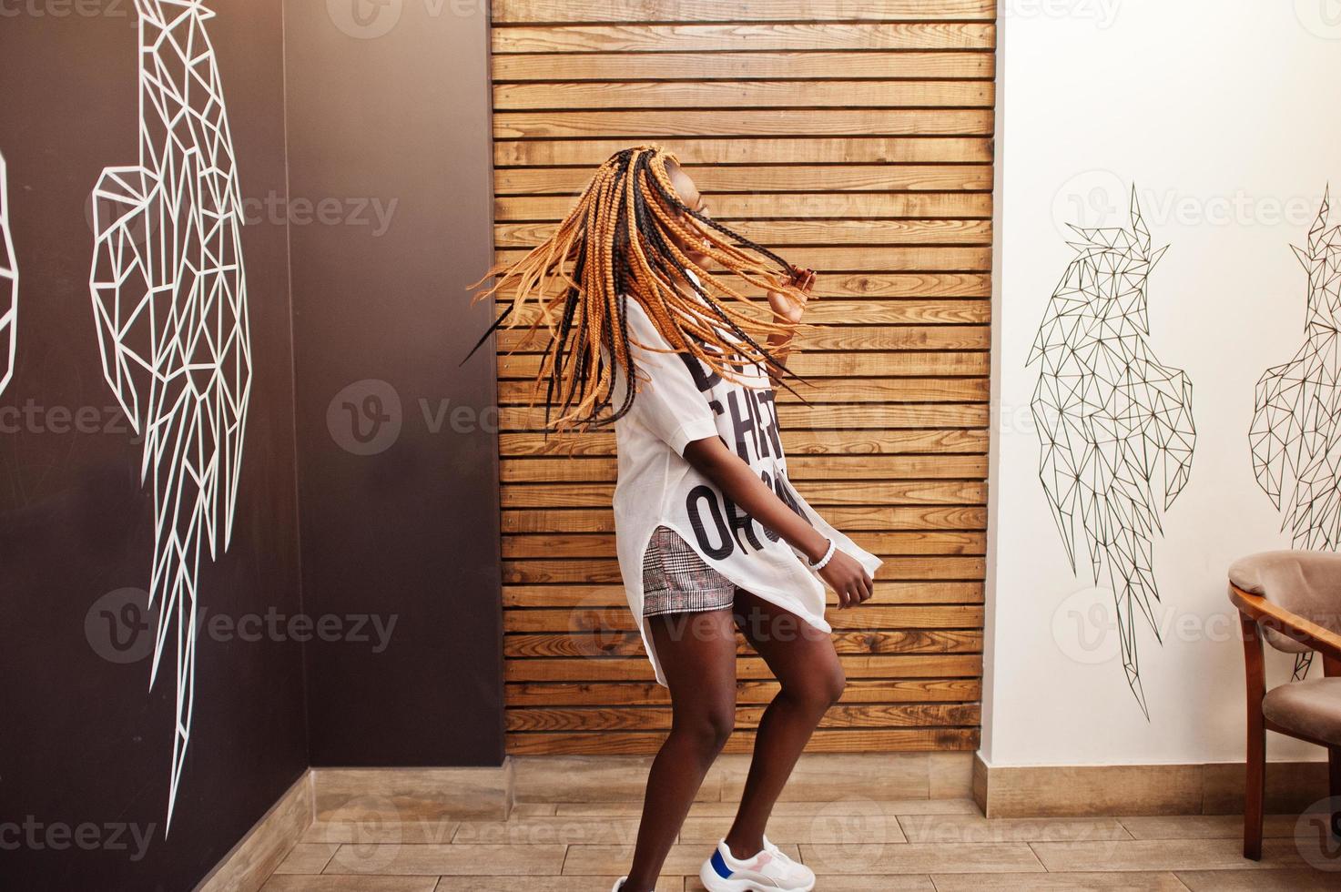 linda mulher africana em roupas casuais elegantes posando contra a parede de asas de anjo. ela movendo seus dreadlocks de cabelo. foto