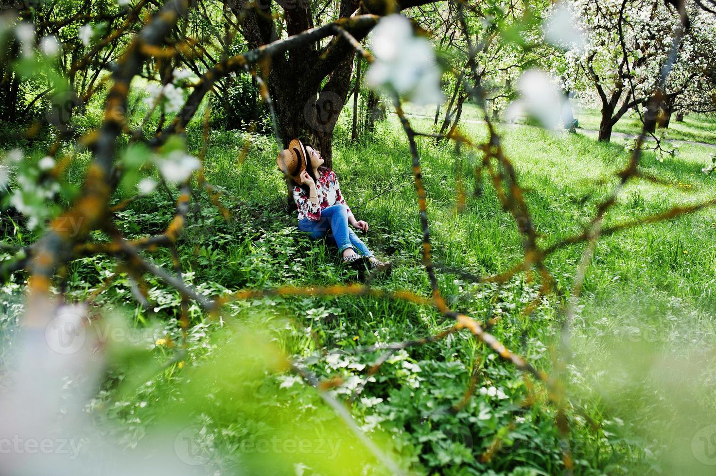 retrato de primavera de menina morena de óculos cor de rosa e chapéu no jardim de flor verde. foto