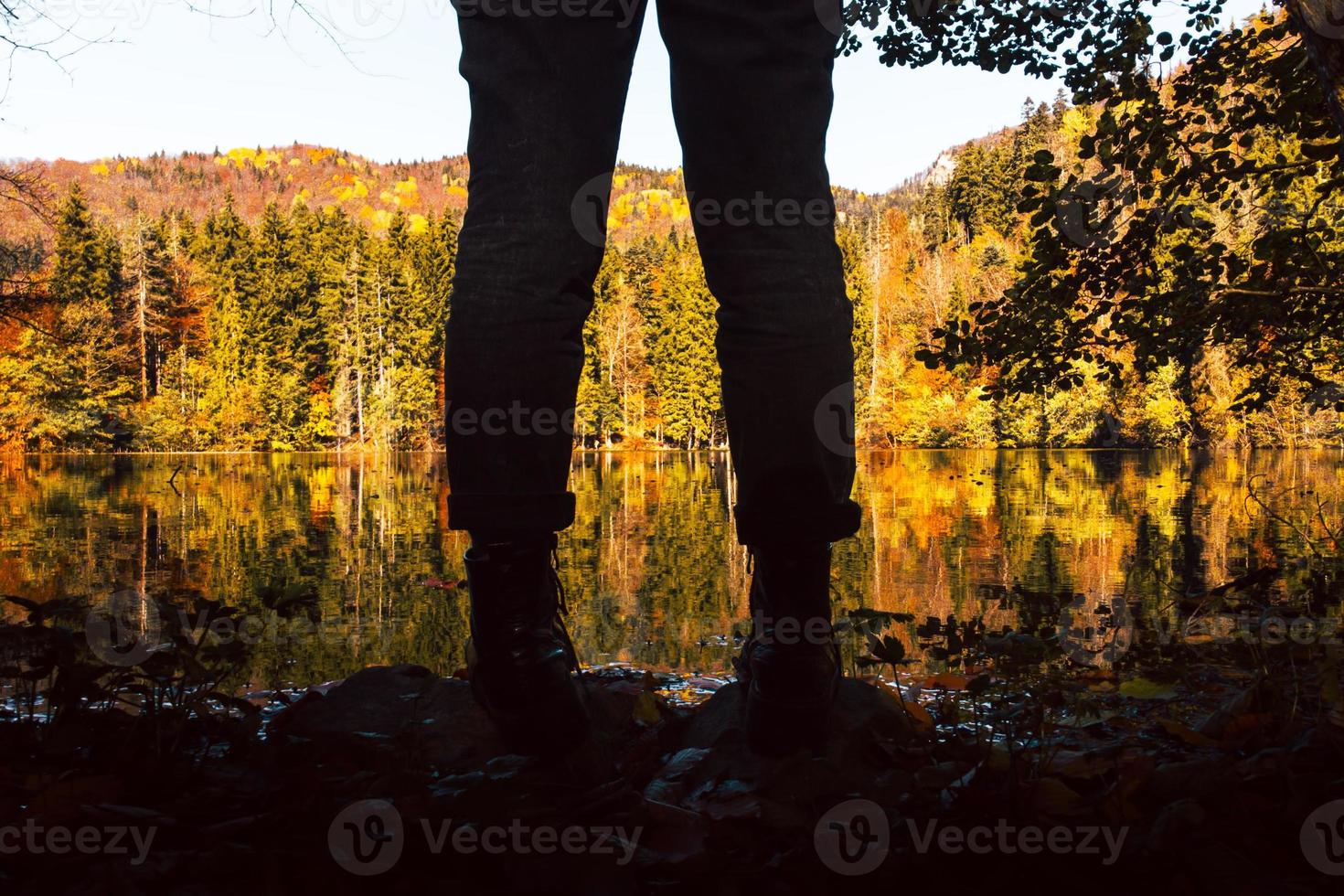 feche a silhueta de visão de baixo ângulo de pernas femininas e botas pelo lago cênico com ao ar livre na natureza do outono. vestuário na natureza e conceito de moda outono foto