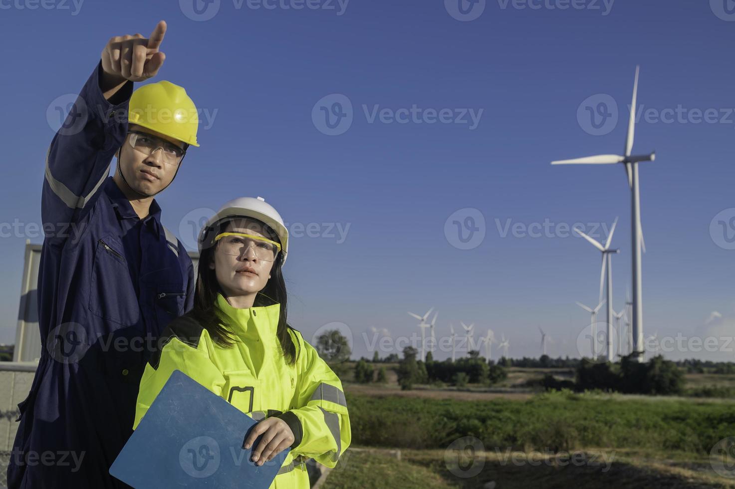 dois engenheiros trabalhando e segurando o relatório na estação de gerador de energia de turbina eólica na montanha, tailândia, técnico homem e mulher discutem sobre trabalho foto