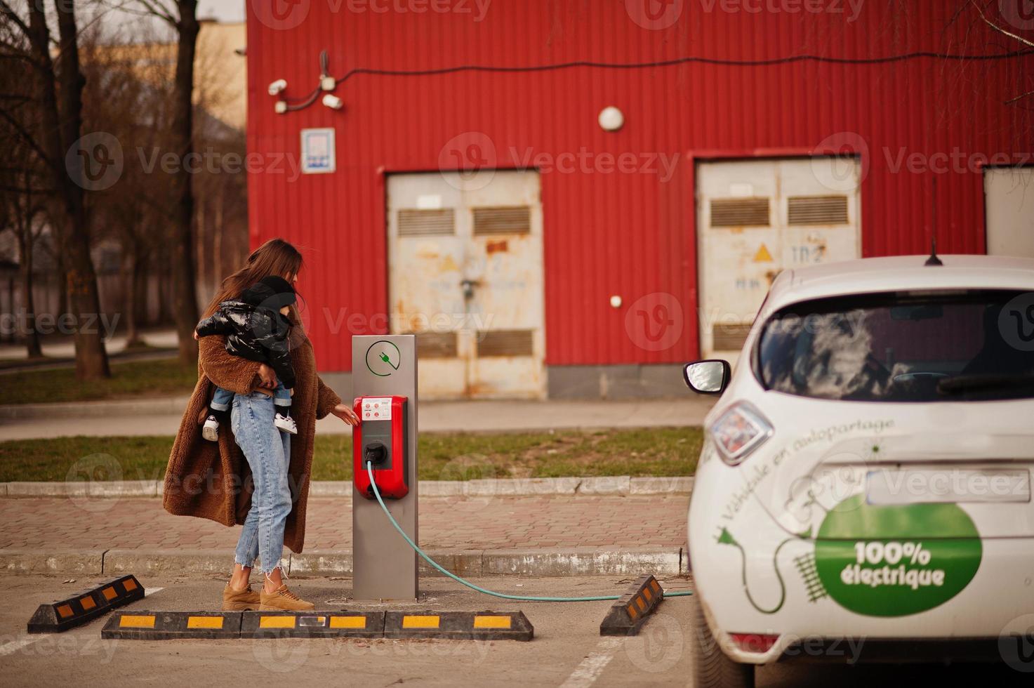 jovem mãe com criança carregando carro elétrico no posto de gasolina elétrico. foto