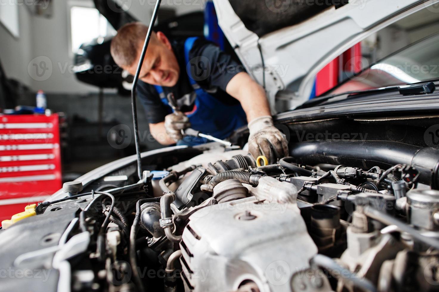 tema de reparação e manutenção de automóveis. mecânico de uniforme trabalhando em auto serviço, verificando o motor. foto