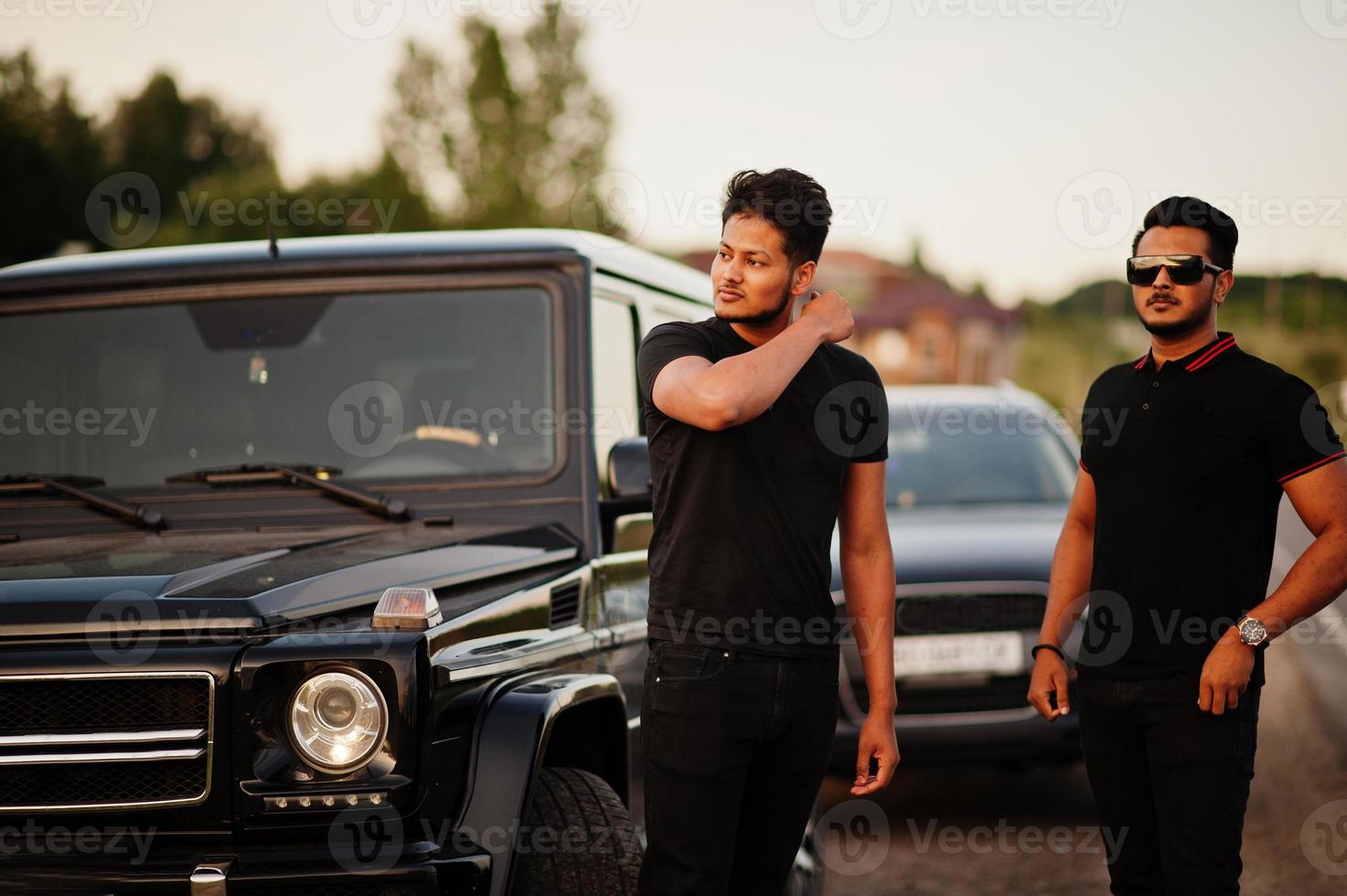 dois irmãos asiáticos vestem todo preto posando perto de carros suv. foto