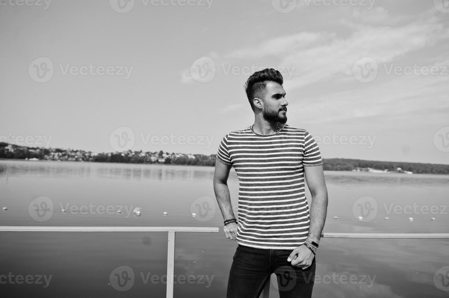 modelo de homem de barba árabe alto bonito na camisa despojada posou ao ar livre no cais do lago. cara árabe na moda. foto