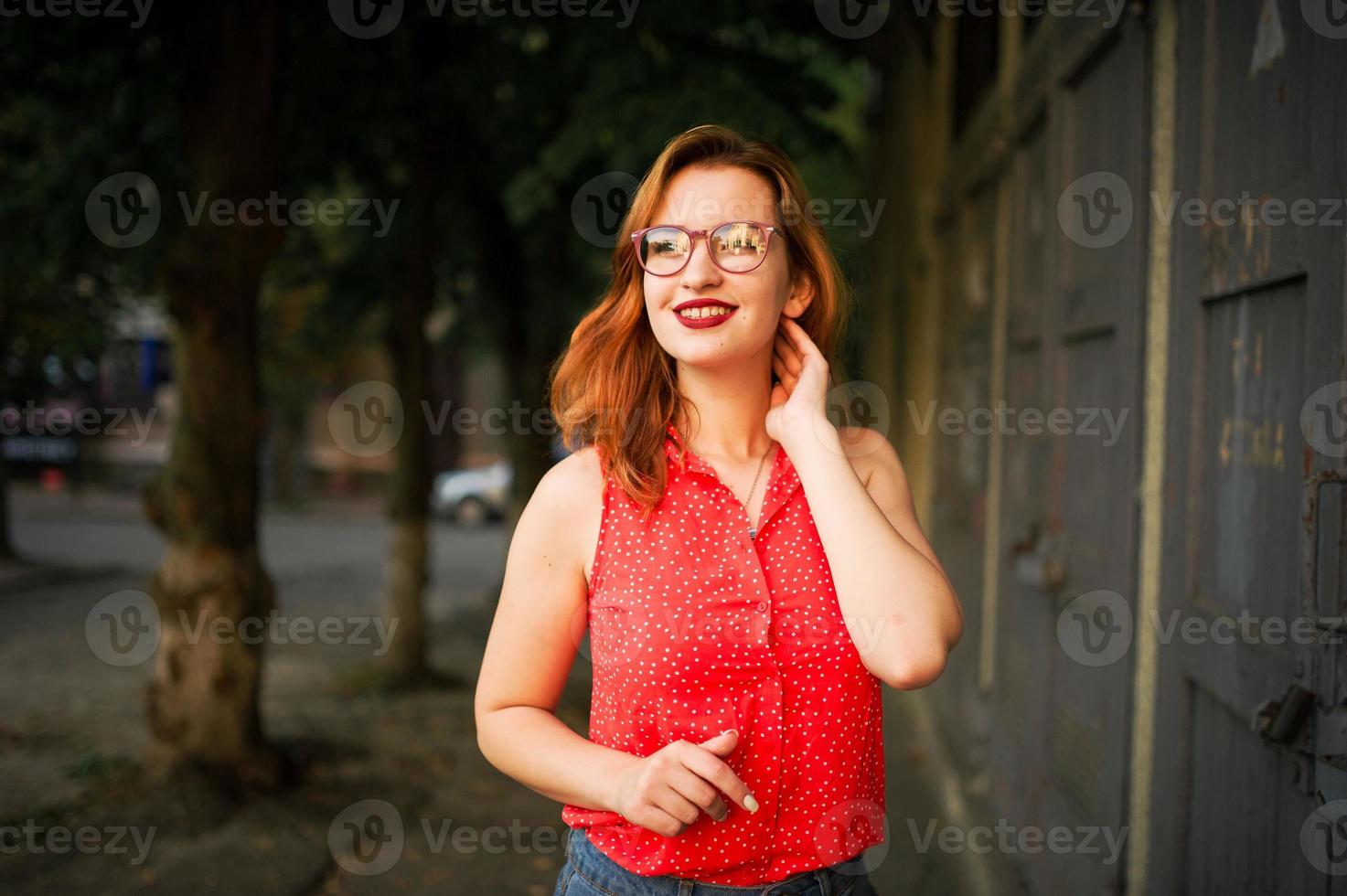 mulher ruiva atraente em óculos, use blusa vermelha e saia jeans posando. foto