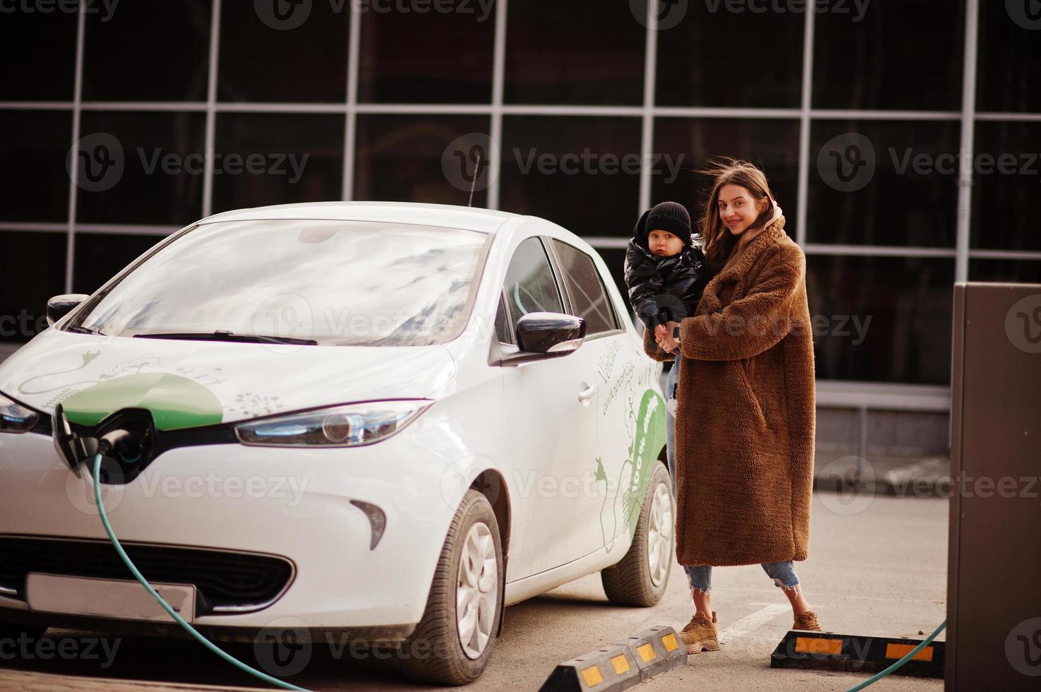 jovem mãe com criança carregando carro elétrico no posto de gasolina elétrico. foto