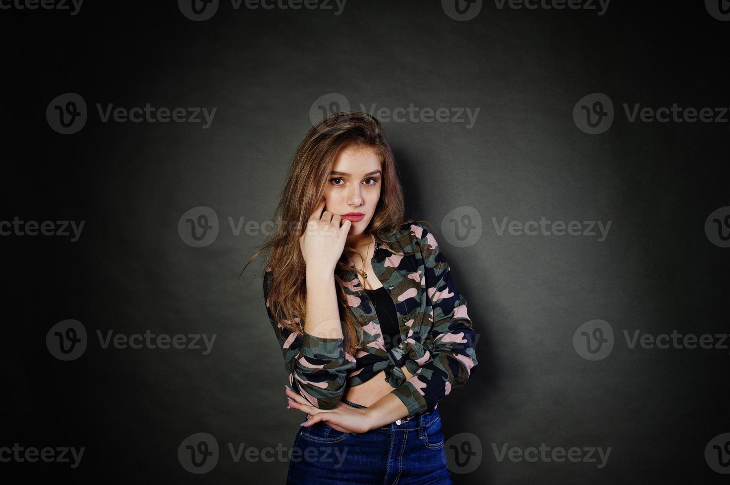 menina morena bonita usa calça jeans e camisa militar, posando no estúdio contra um fundo cinza. retrato de modelo de estúdio. foto