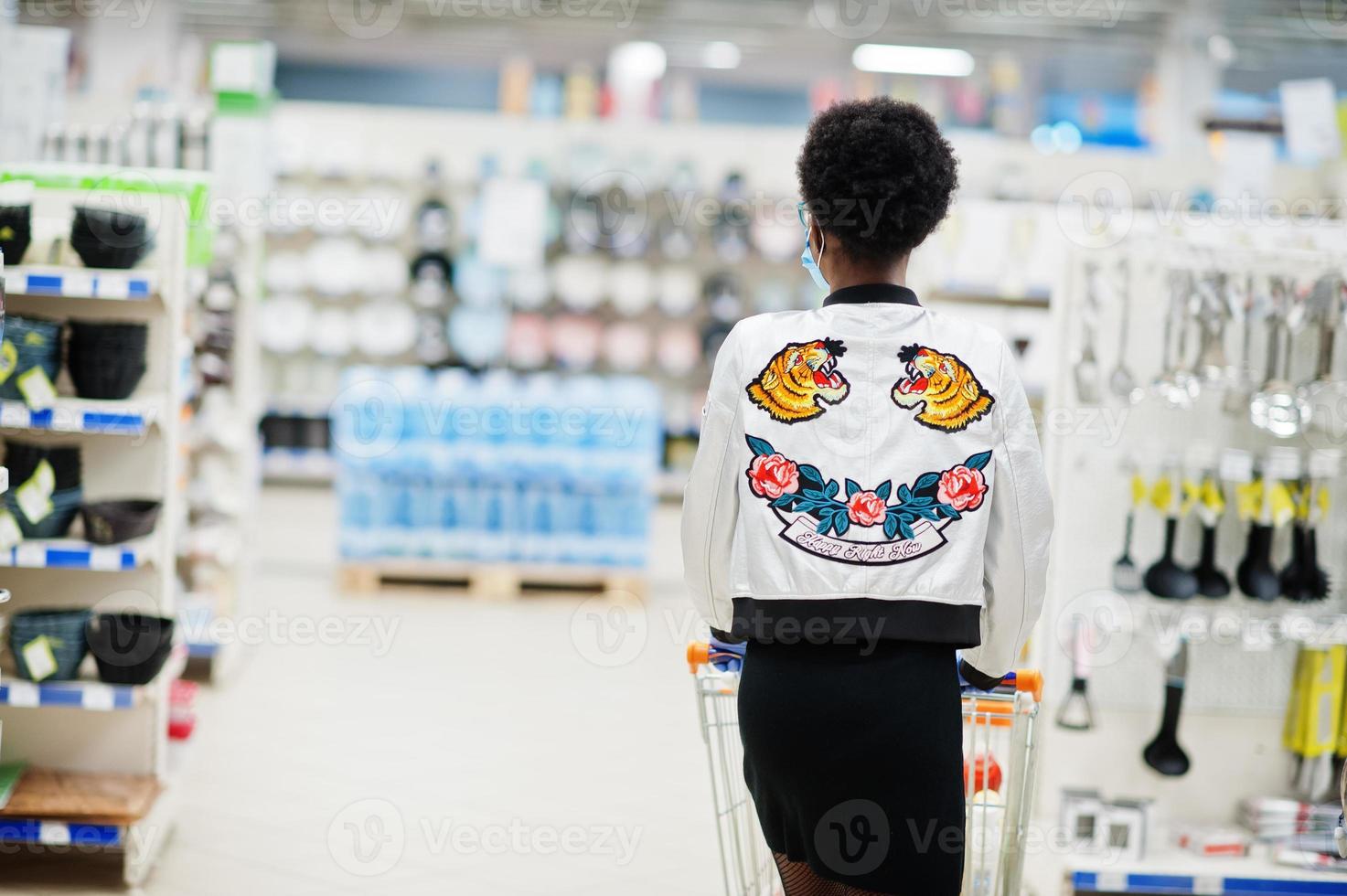 mulher africana usando máscara médica descartável e luvas fazendo compras no supermercado durante o surto de pandemia de coronavírus. tempo epidêmico. foto