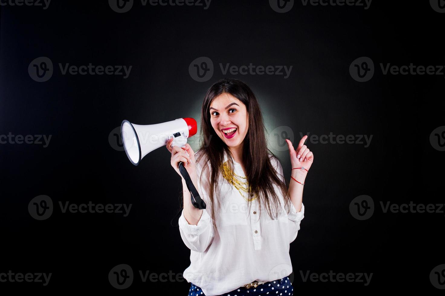 retrato de uma jovem de calça azul e blusa branca posando com megafone no estúdio. foto