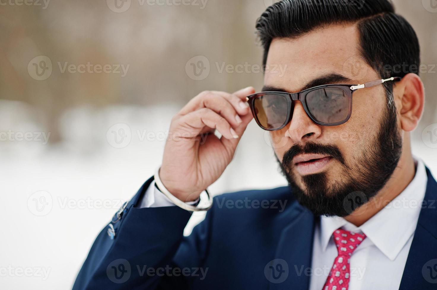 Feche o retrato do homem de negócios elegante barba indiana de terno e óculos de sol posou no dia de inverno ao ar livre. foto