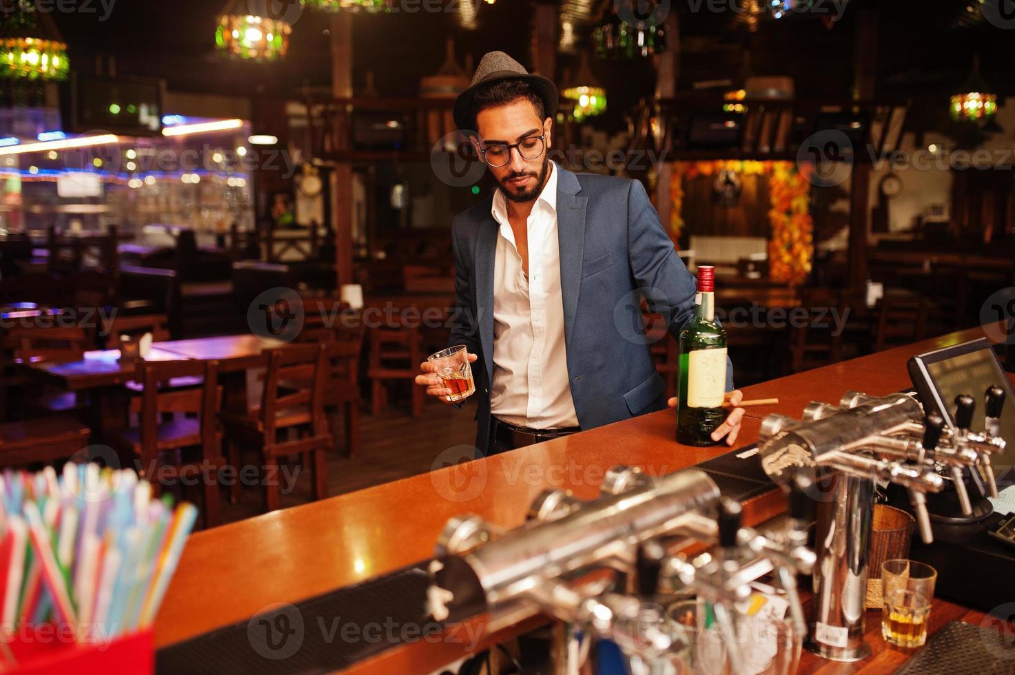 homem árabe bem vestido bonito com copo de uísque e charuto posou no pub. foto