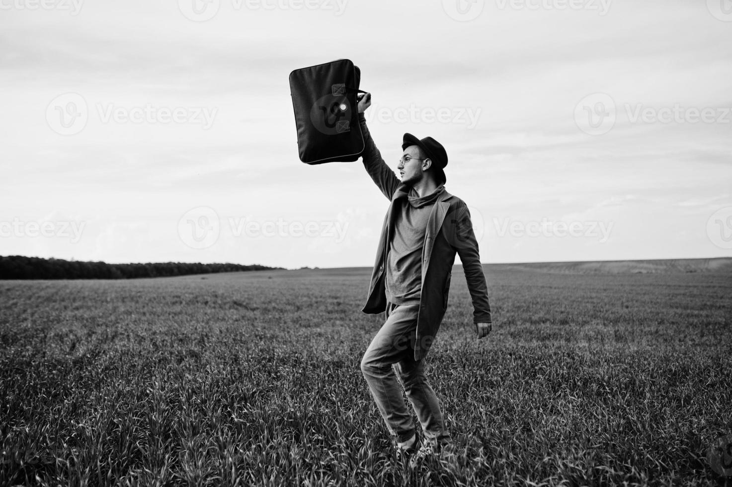 homem elegante de óculos, jaqueta marrom e chapéu com bolsa posou em campo verde. foto