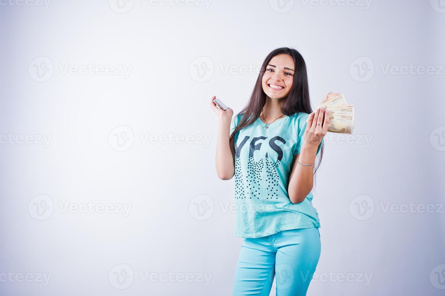 retrato de uma garota atraente em camiseta azul ou turquesa e calças posando com muito dinheiro na mão. foto